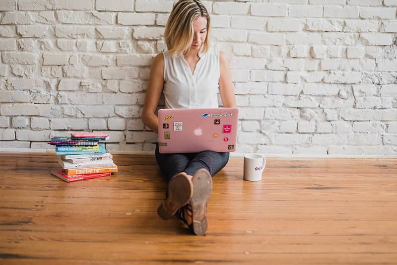 A lady sitting on the floor with a pink laptop on her legs.