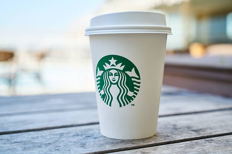 A starbucks coffee cup outside on a woodern table