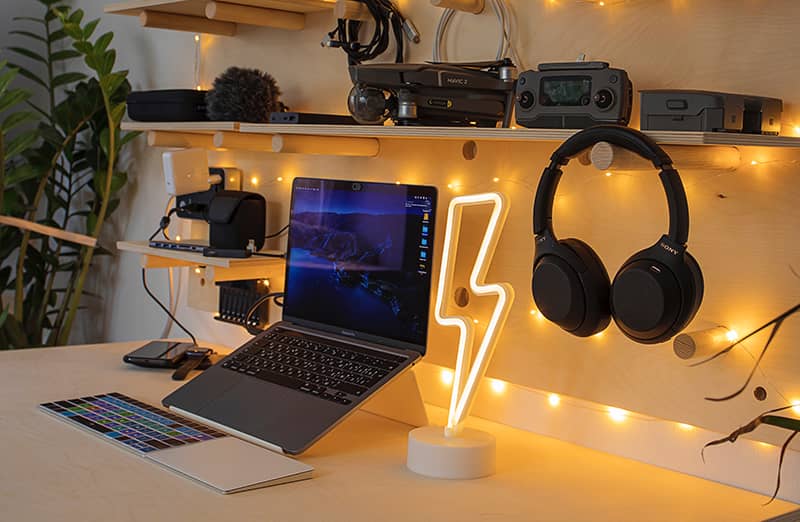 A desk with a lightening bolt light and laptop surrounded with other tech gadgets on a shelf