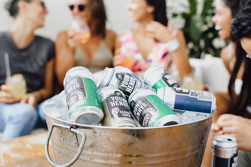 A ice bucket with cans of cider with four friends in the background