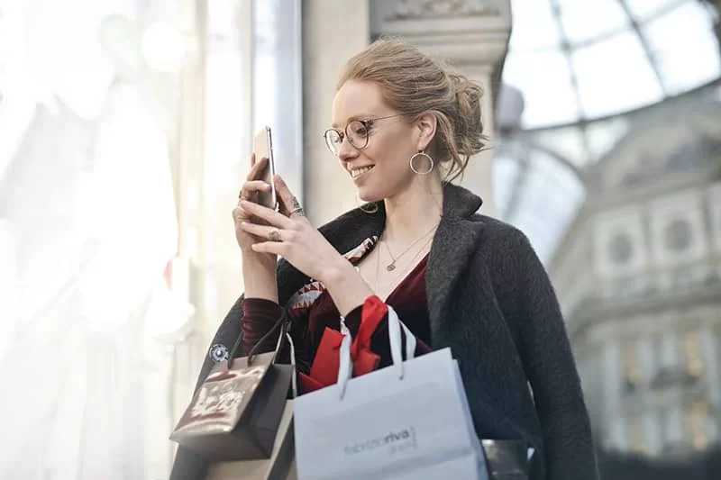 A girl looking at her mobile phone while shopping with her shopping bags in hand