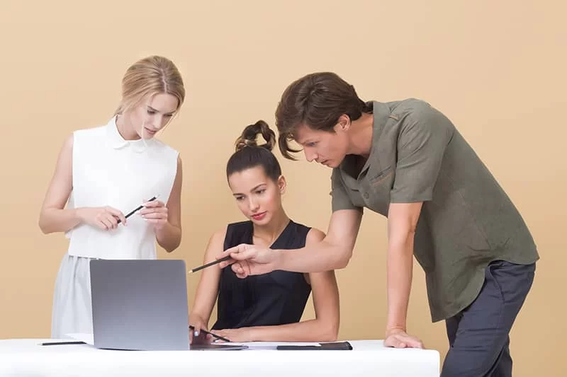 A man pointing at a laptop screen with two girls watching.