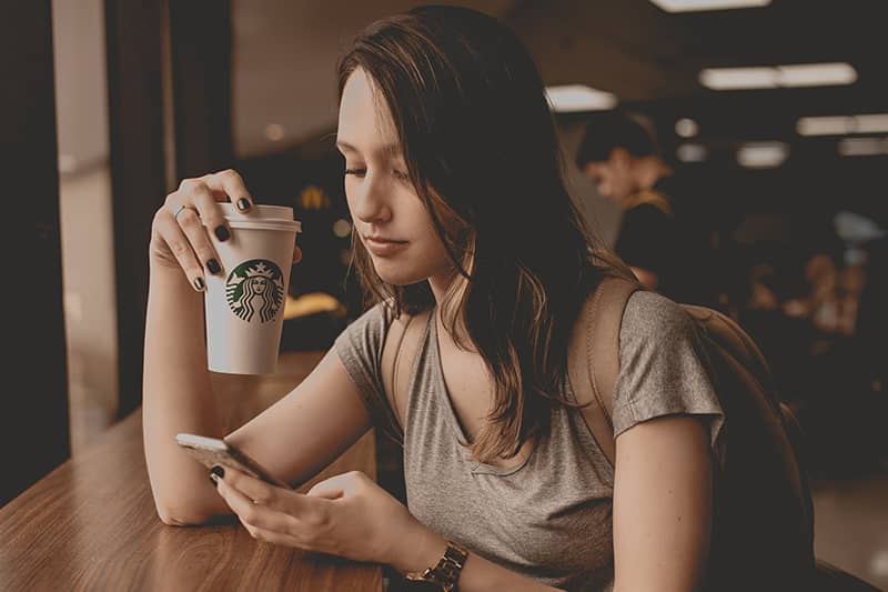 A girl sitting at Starbucks drinking a coffee and looking at her mobile phone