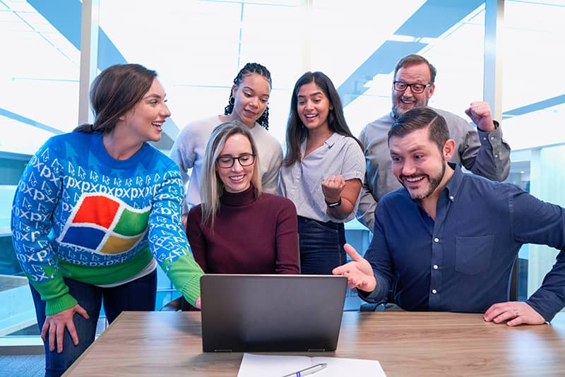 The Microsoft team members sitting and standing around a laptop on a desk