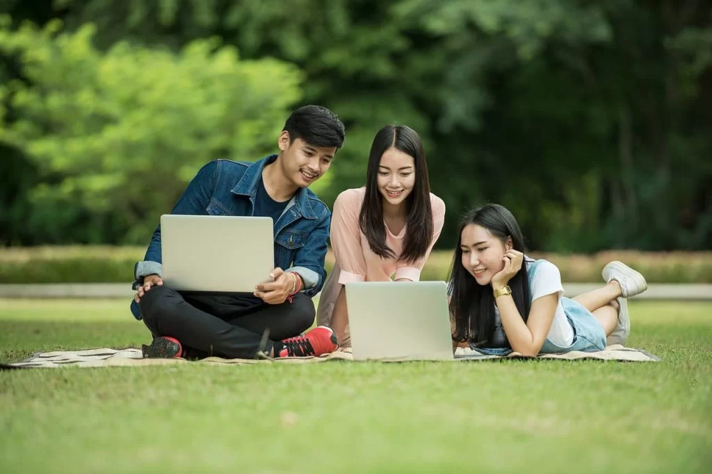 A group of three teenagers sitting outside on the lawn looking at a laptop screen.