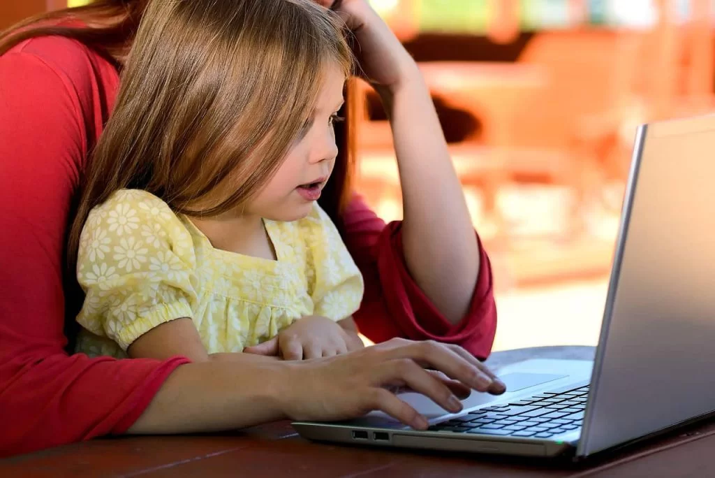 A young girl sitting on her mothers lap looking at a laptop screen