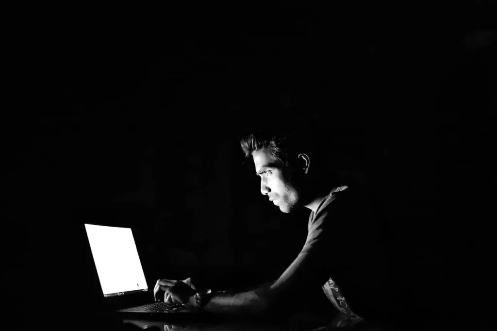 A person sitting in a dark room looking at their laptop screen.