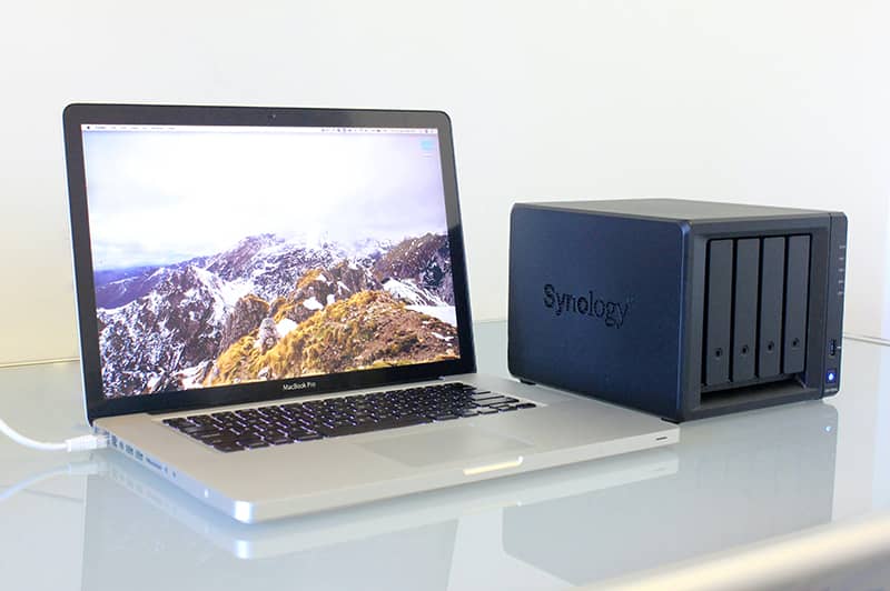 A MacBook laptop with a Synology 4-Bay NAS drive on the desk