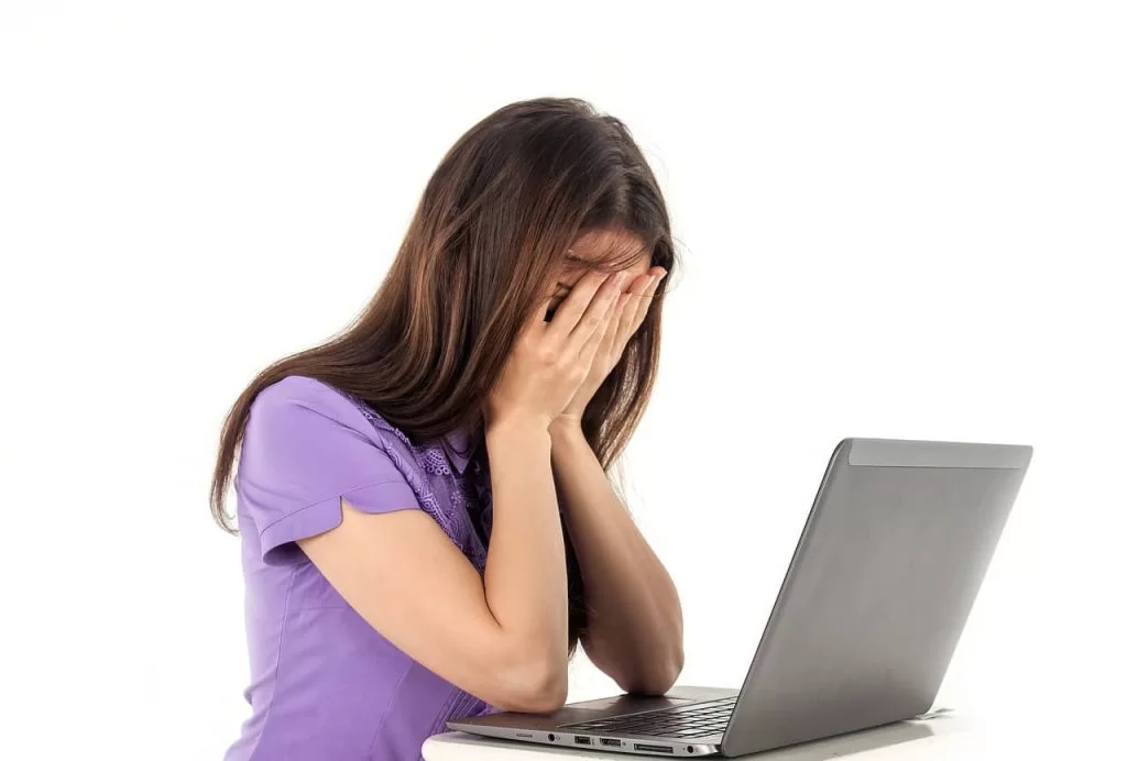 A girl crying into her hands in front of her laptop